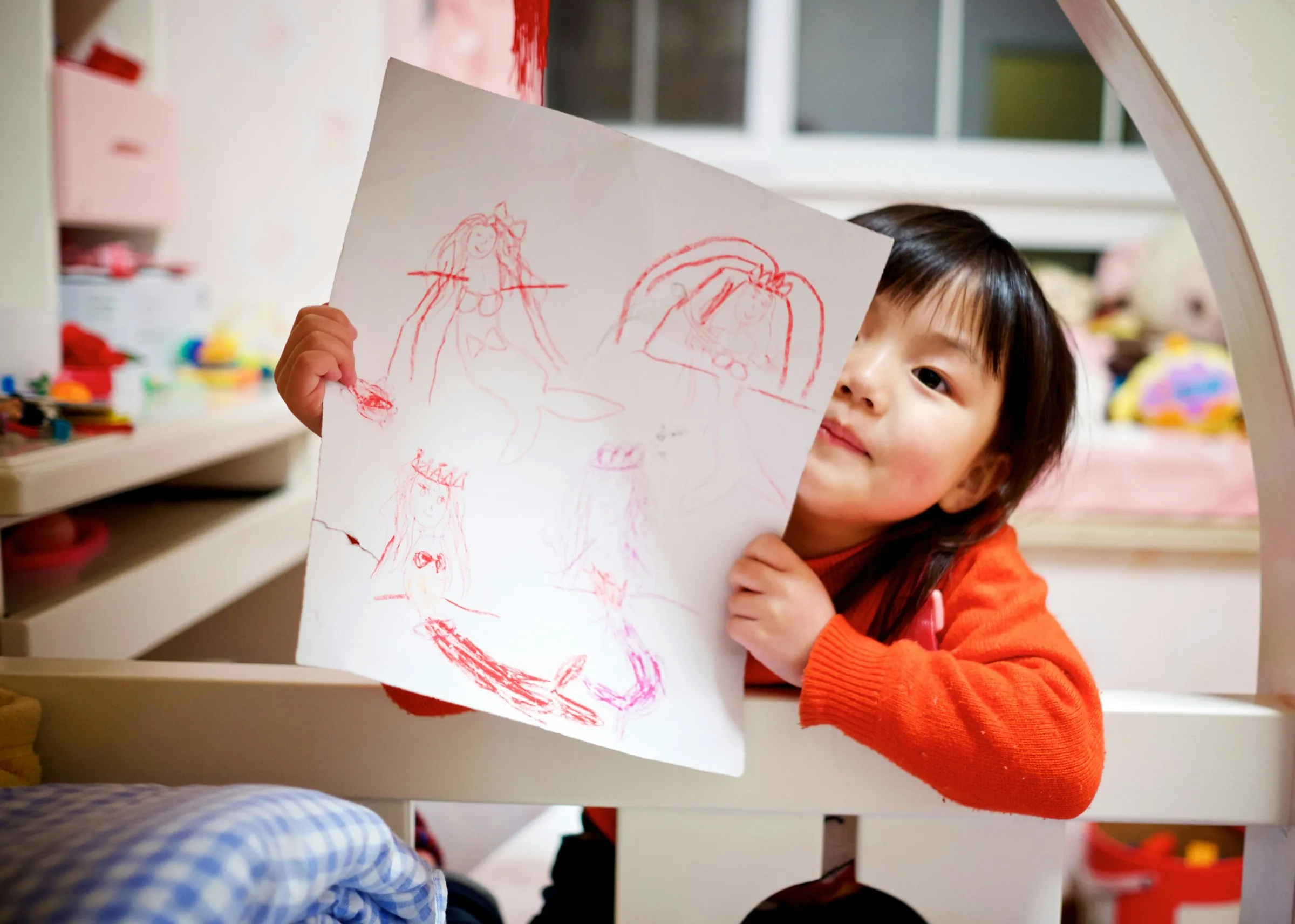 Young girl proudly holding up her crayon drawing, recognizing children's strengths and interests