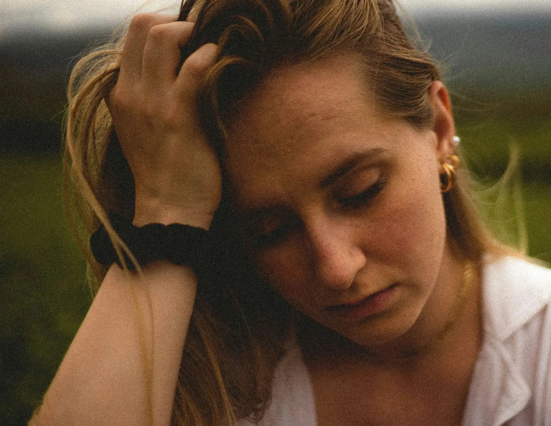 Woman looking down with her hand in her hair, people-pleasing and boundaries therapy
