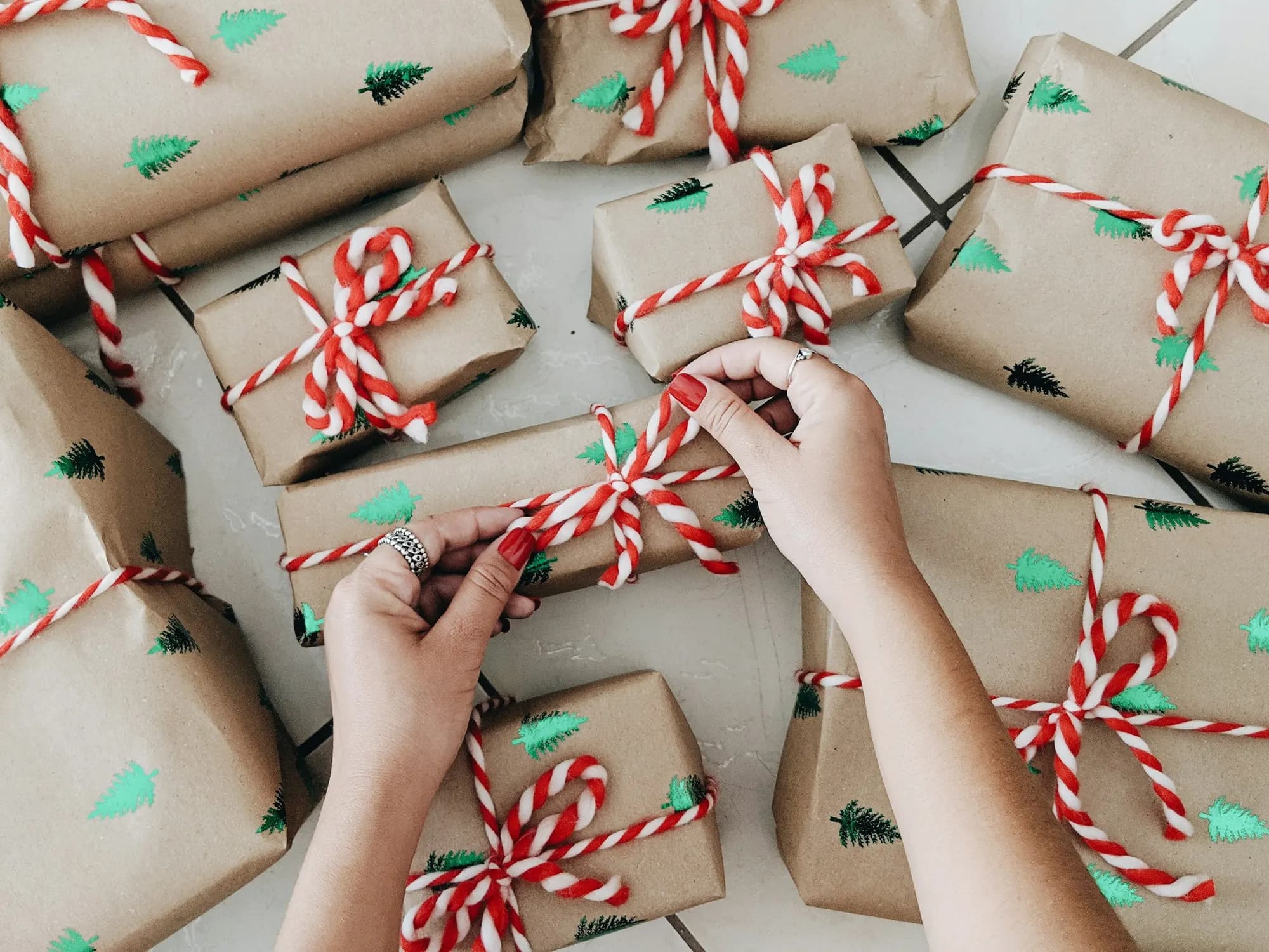 Hands tying ribbon on a table full of wrapped holiday gifts, the holiday mental load